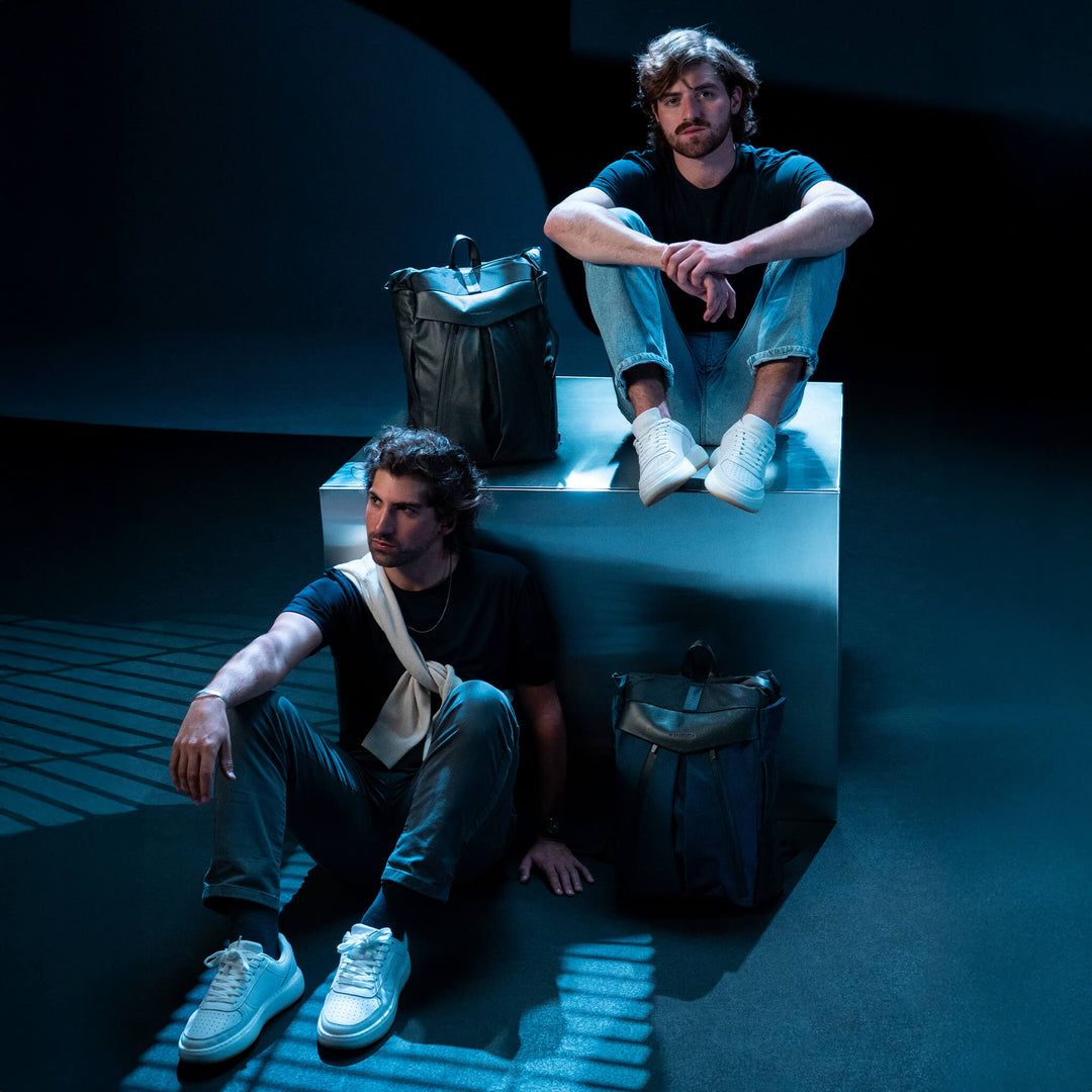 Two men sitting on a platform with bags around them in a dark setting