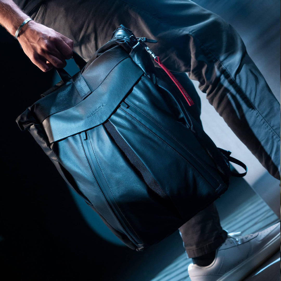 Person holding a black backpack with a red zipper on a reflective surface