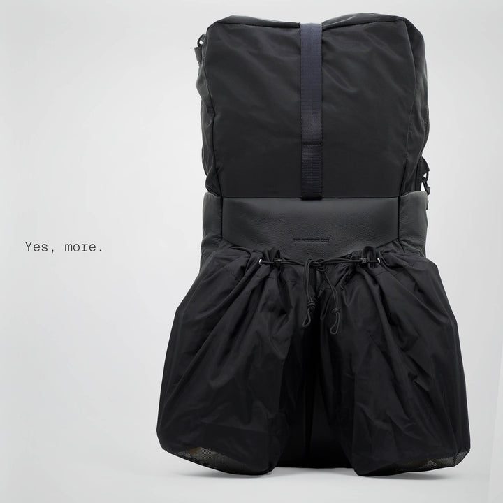 Black backpack with a drawstring at the bottom on a light gray background