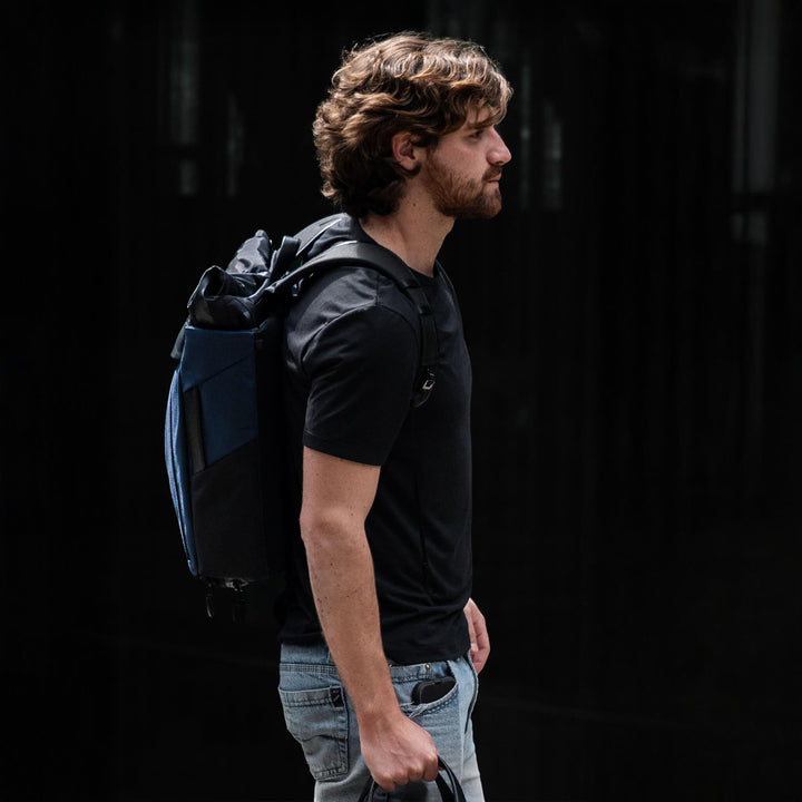 Man with a blue backpack walking against a dark background